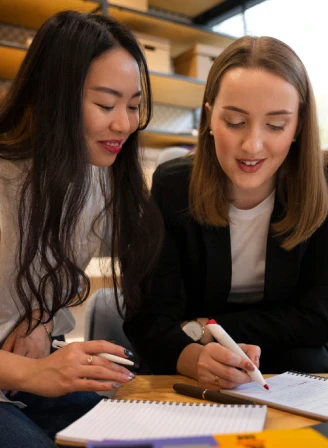 two girls discussing and writing a note down